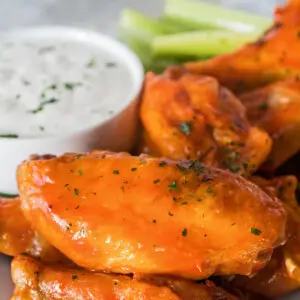 Air fryer frozen chicken wings with buffalo sauce coating and a side of ranch and veggies.