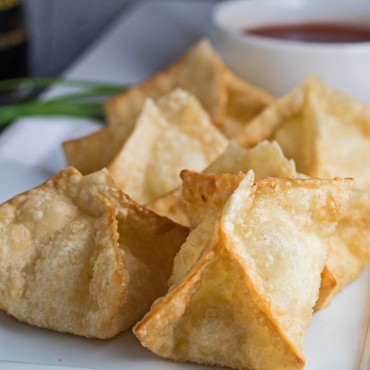 Fried crab rangoons on white plate with sweet n sour sauce.