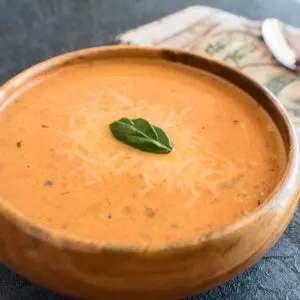 Super creamy roasted tomato basil soup served in wooden bowl.