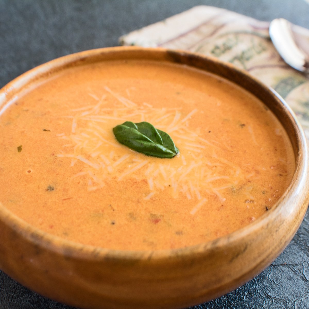 Sopa super cremosa de tomate assado com manjericão servida em tigela de madeira.