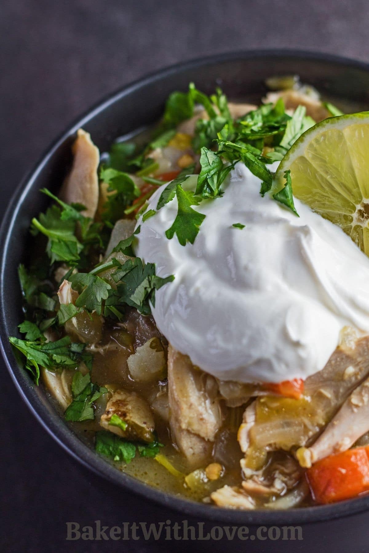 Green chile chicken stew topped with sour cream and cilantro in black bowl.