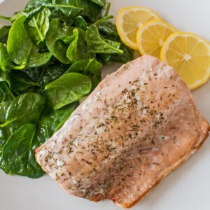 Saumon poêlé servi avec des légumes verts fanés et des tranches de citron.