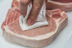Tepuk-tepuk potongan daging babi yang tebal hingga kering sebelum dibumbui.