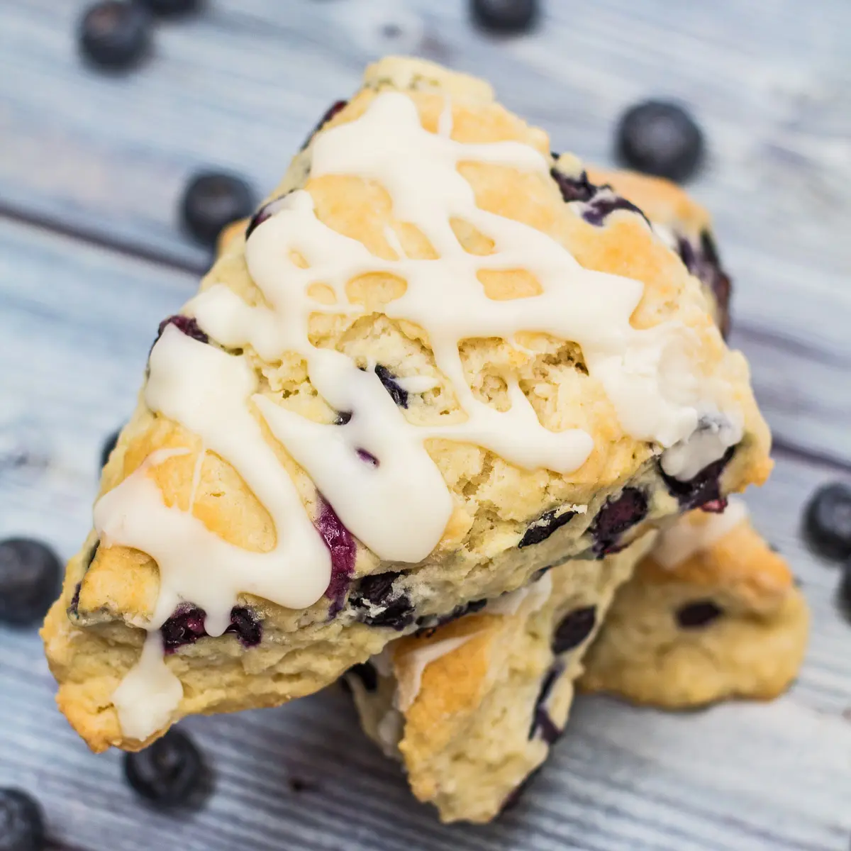 Blueberry cream cheese scones with icing and blueberries in background.