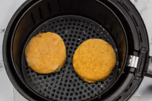 Frozen chicken patties placed into air fryer basket.