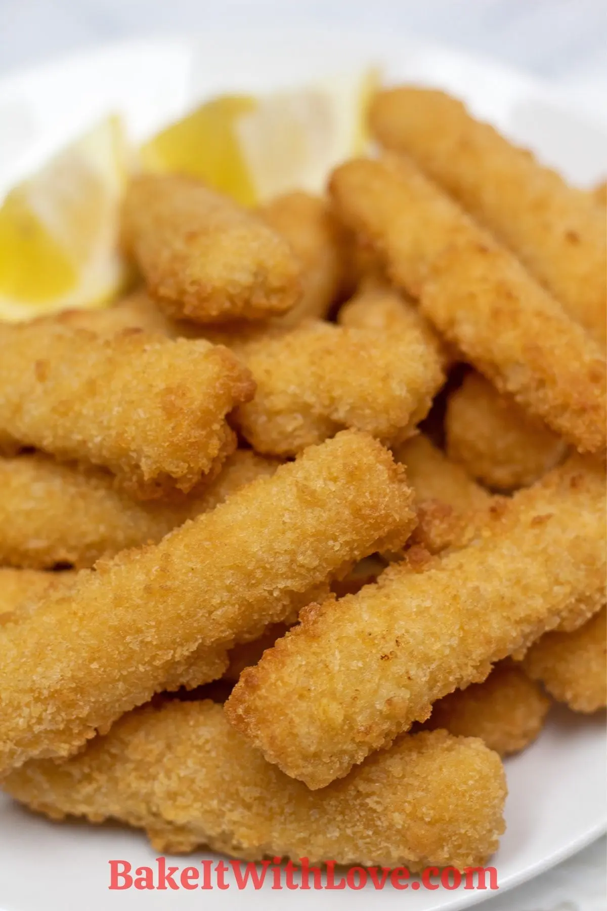 Fish sticks on a plate with lemon wedges.