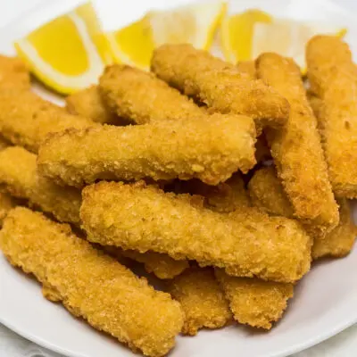 Air fryer frozen fish sticks on white plate with lemon wedges.