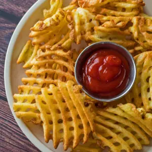 Waffle Fries cooked in an air fryer and served on plate with ketchup.