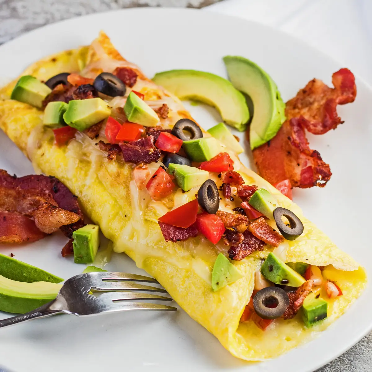 Californien omelet med bacon og avocado på en hvid plade.