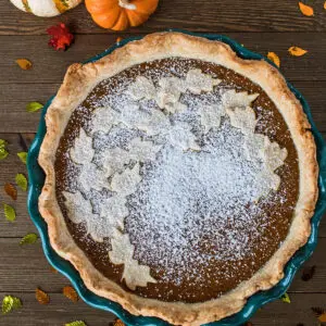 Pumpkin Pie in green pie plate on wooden background.