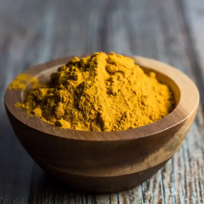 Loose ground turmeric in wooden bowl on wooden grain background.