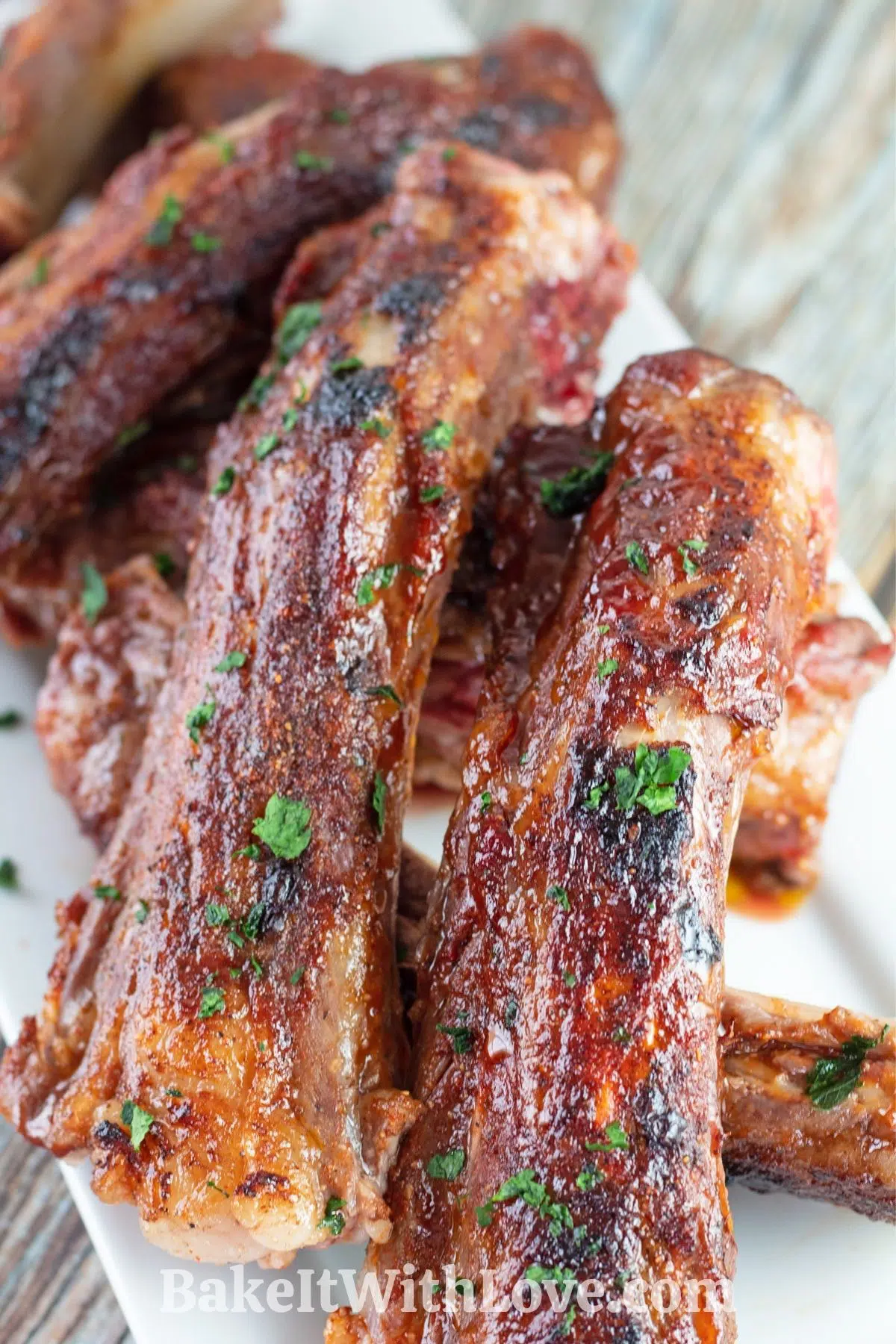 BBQ baked beef back ribs stacked on white plate with wooden grain background.