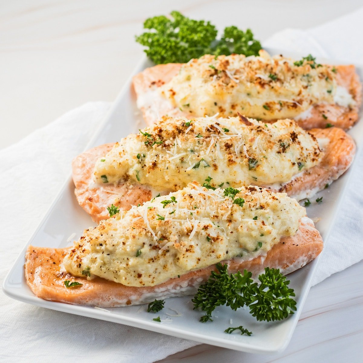 Crab stuffed salmon served on white plate garnished with fresh parsley.