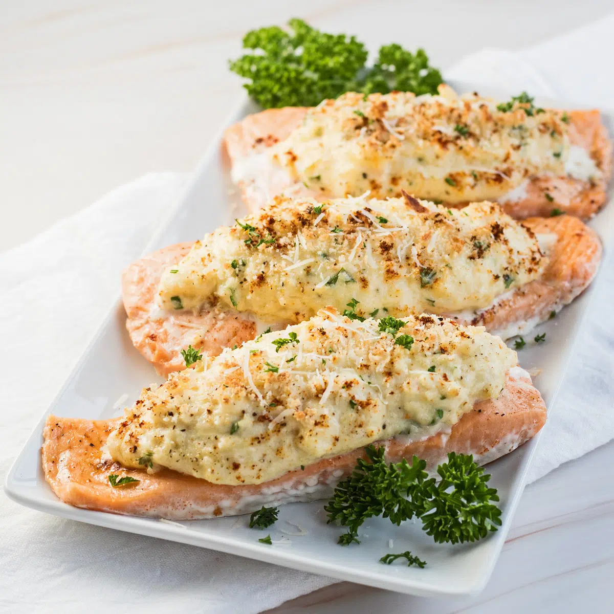 Crab stuffed salmon served on white plate garnished with fresh parsley.