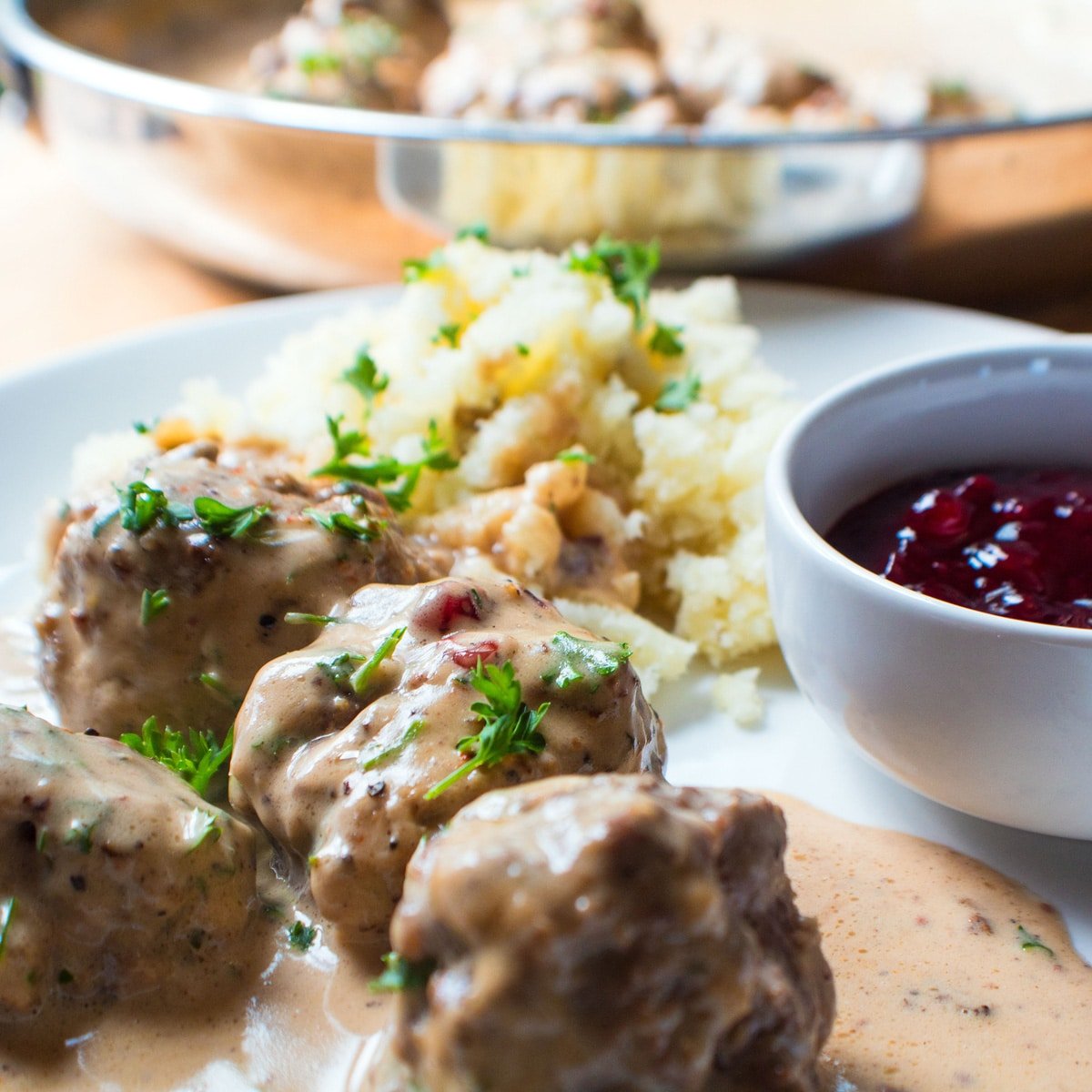 Polpette svedesi abbondanti servite con sugo di carne e marmellata di mirtilli rossi su un piatto bianco.