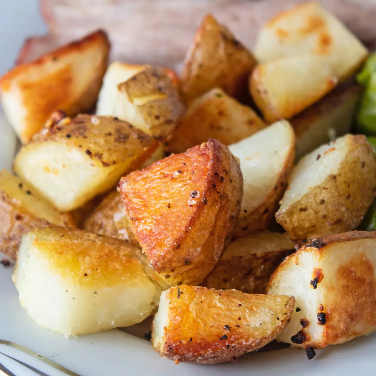 Krokante oven geroosterde aardappelen geserveerd op schotel met gebraden vlees en groenten.