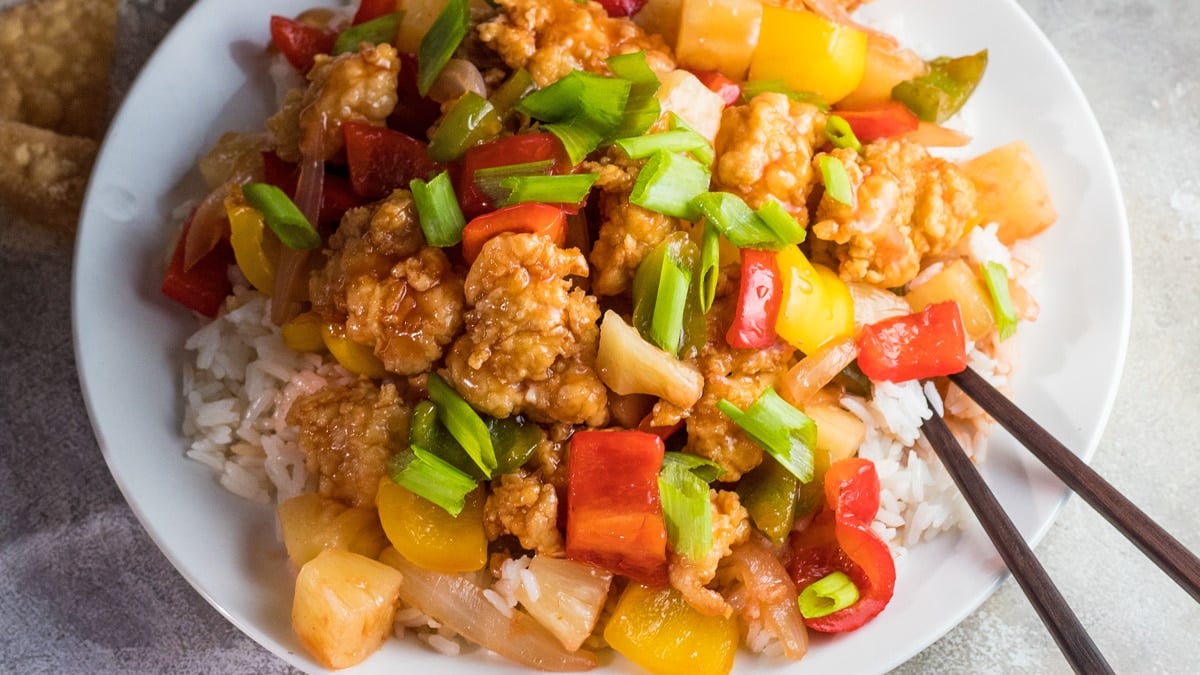 Tasty sweet and sour chicken served over rice on a white plate.
