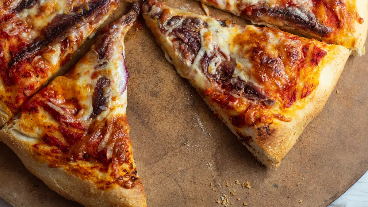 Sliced anchovy pizza on pizza stone.