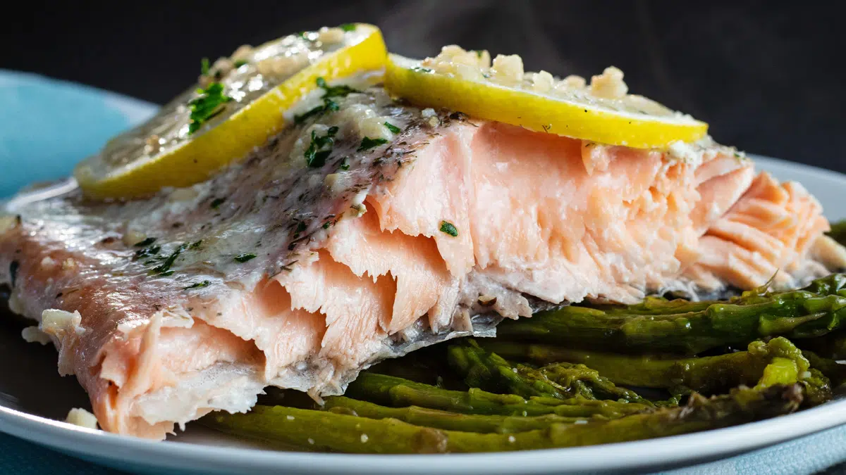 Baked salmon in foil served with asparagus on white plate.