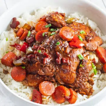 Rich and flavorful brown stew chicken served over rice in white bowl.