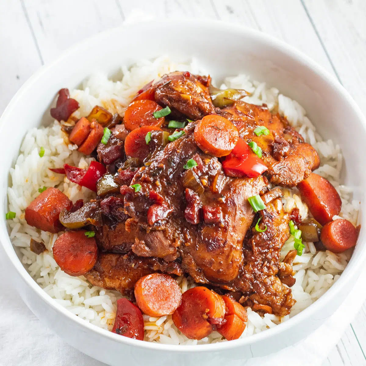 Rich and flavorful brown stew chicken served over rice in white bowl.