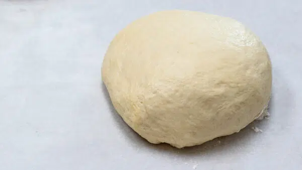 Shaped pizza dough round ready to rise on parchment paper.
