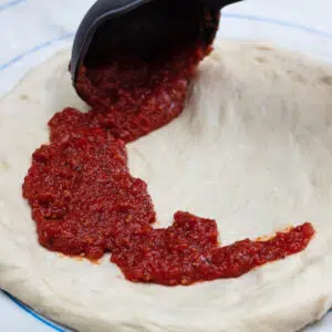 Cooked and blended pizza sauce being applied to pizza dough.