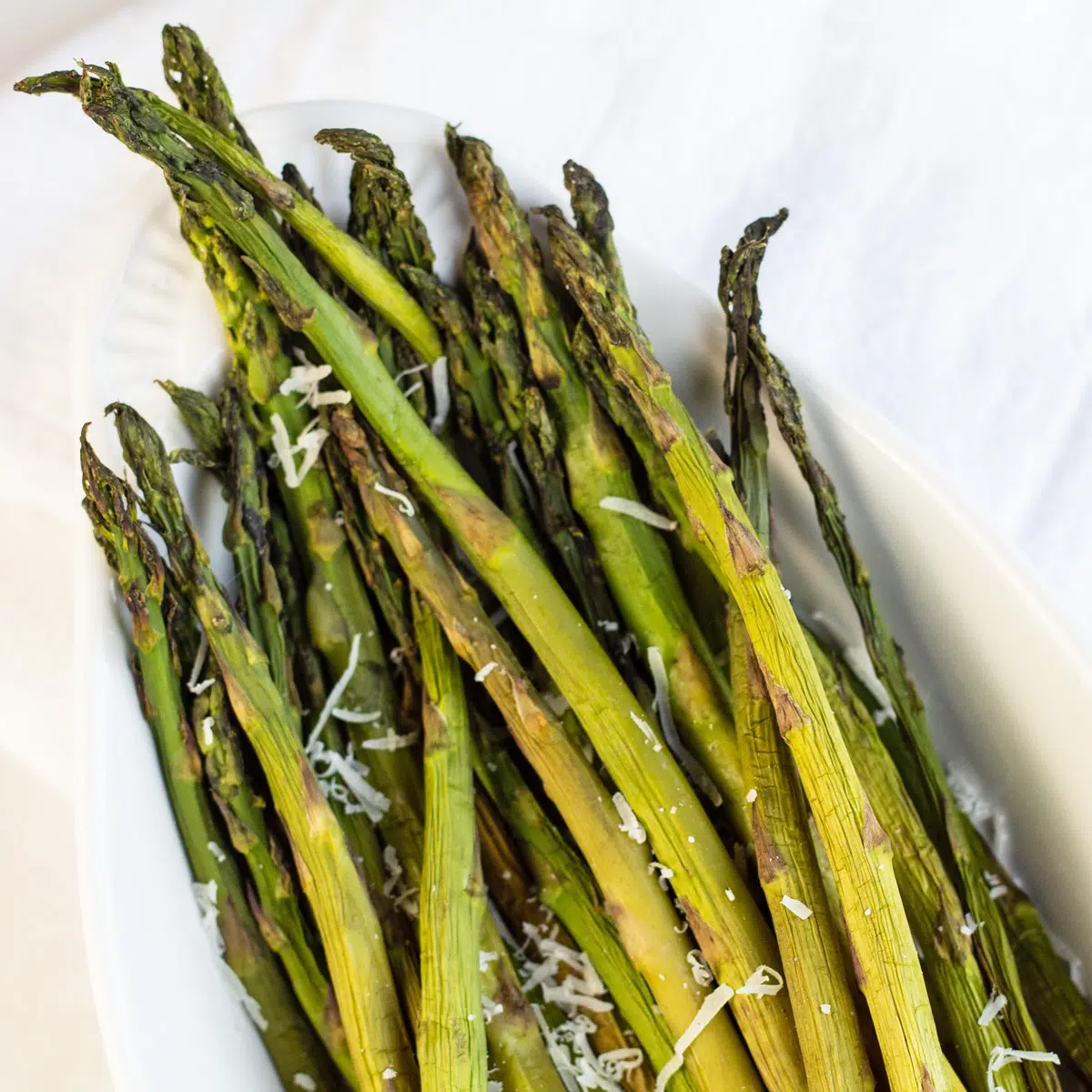 Asparagi affumicati con parmigiano grattugiato fresco su fondo chiaro.