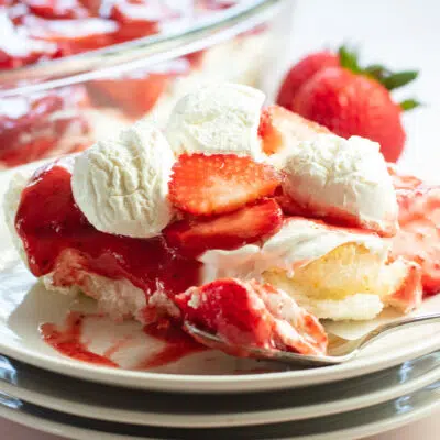 Strawberry angel food lush served on white plate with whipped cream and berries in background.