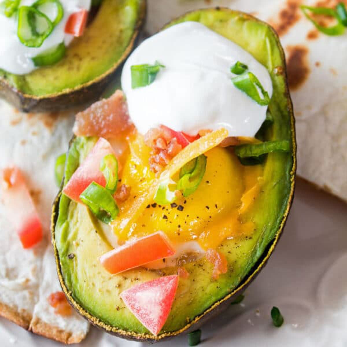 Avocado egg bake loaded with tomatoes, bacon, egg, and cheese, on a table.