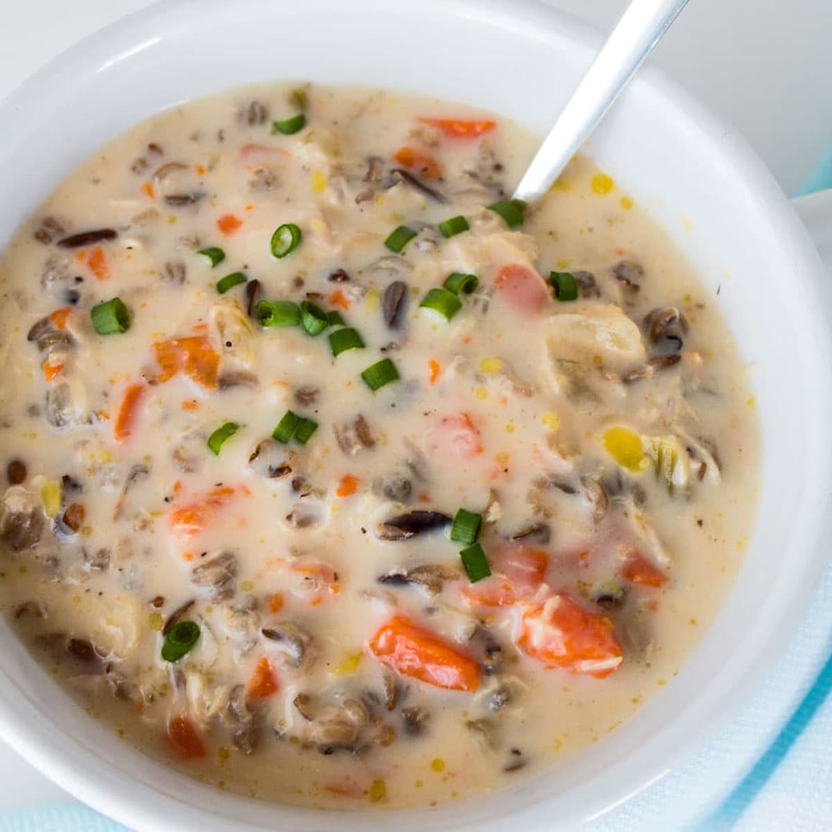 Creamy wild rice soup in a white bowl with green onions on top.