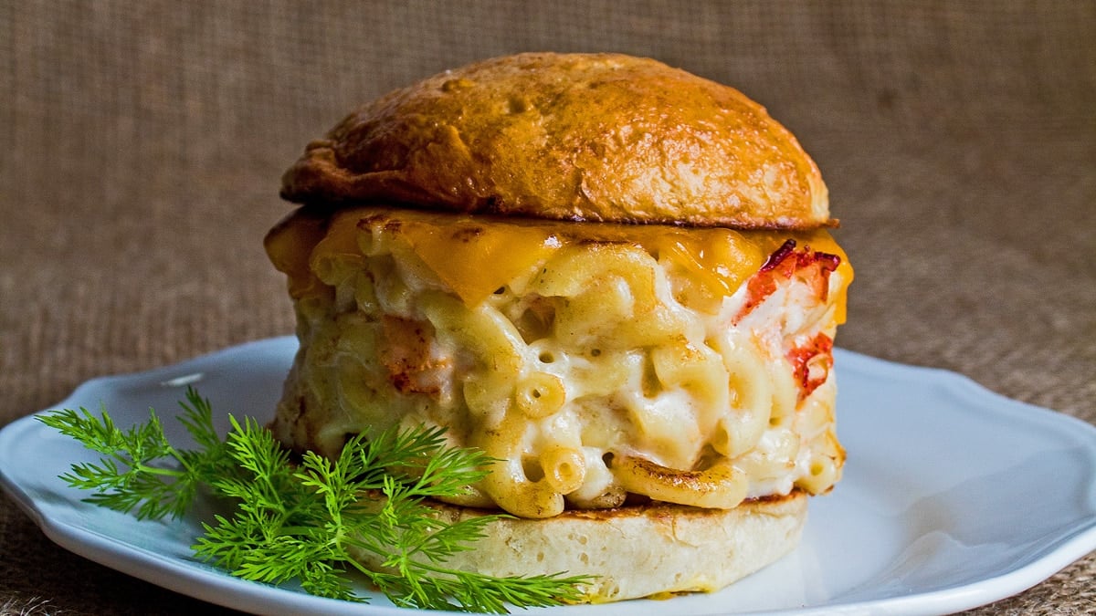 Lobster mac and cheese burger on white plate with dill garnish.