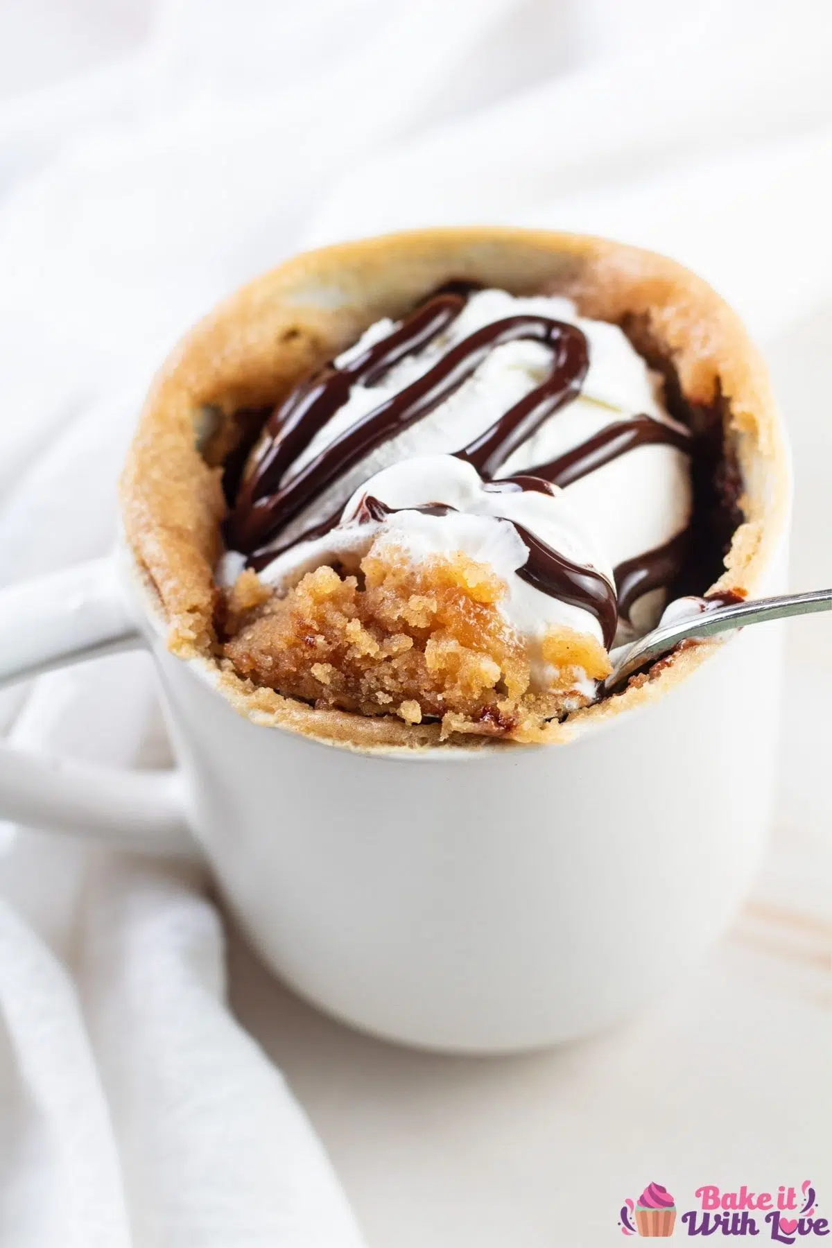 Tall view of the peanut butter mug cake topped with whipped cream and chocolate sauce.
