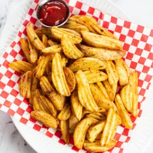 Air fryer frozen potato wedges served in picnic basket with ketchup.