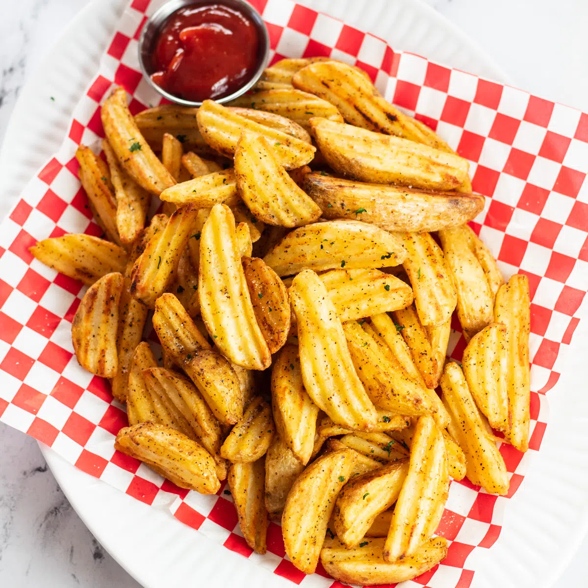 Frysfrysta potatisbitar i luftfryser serveras i picknickkorg med ketchup.
