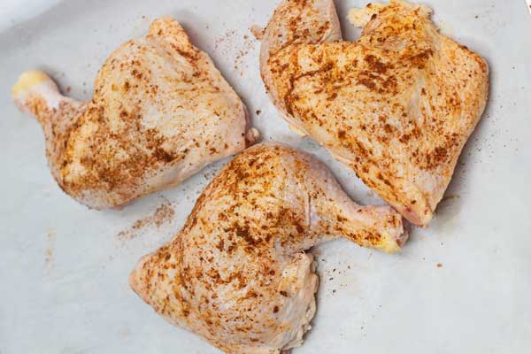 Seasoned chicken quarters on parchment paper lined baking tray.