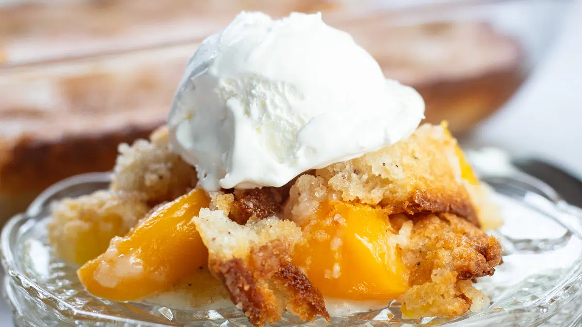 Wide image of the Bisquick peach cobbler served on a glass plate.