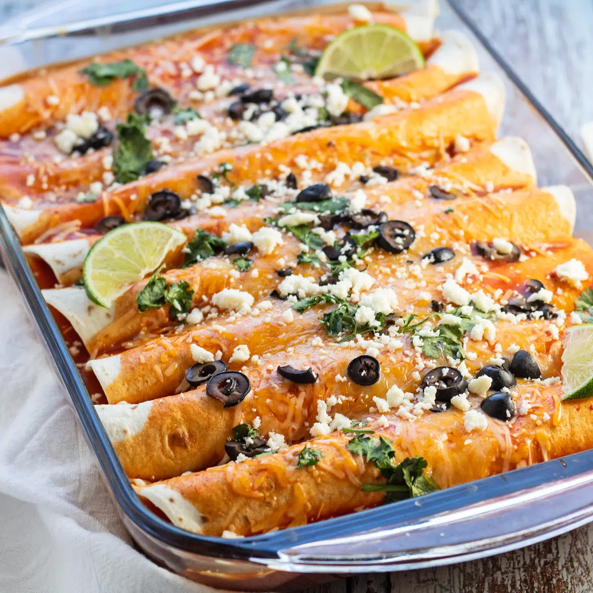Baked cheese enchiladas topped with more cheese, queso fresco, sliced olives, and cilantro.