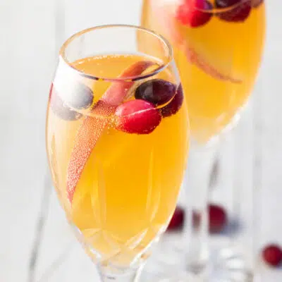Mimosa mocktails in champagne flutes with sliced apple and cranberry garnish.
