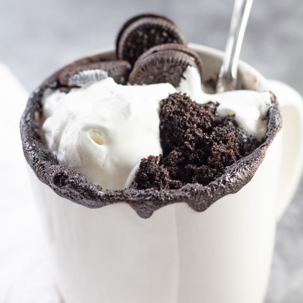 Kue mug Oreo disajikan dengan krim kocok dan tambahan Oreo mini.