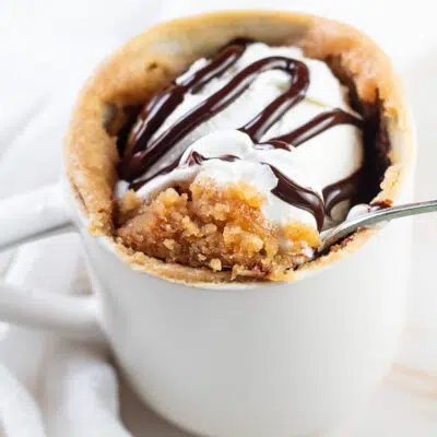 Peanut butter mug cake after cooking in the microwave and topped with whipped cream and chocolate sauce.