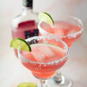 Pink vodka margarita serve din margarita glasses with lemon slice on rim.
