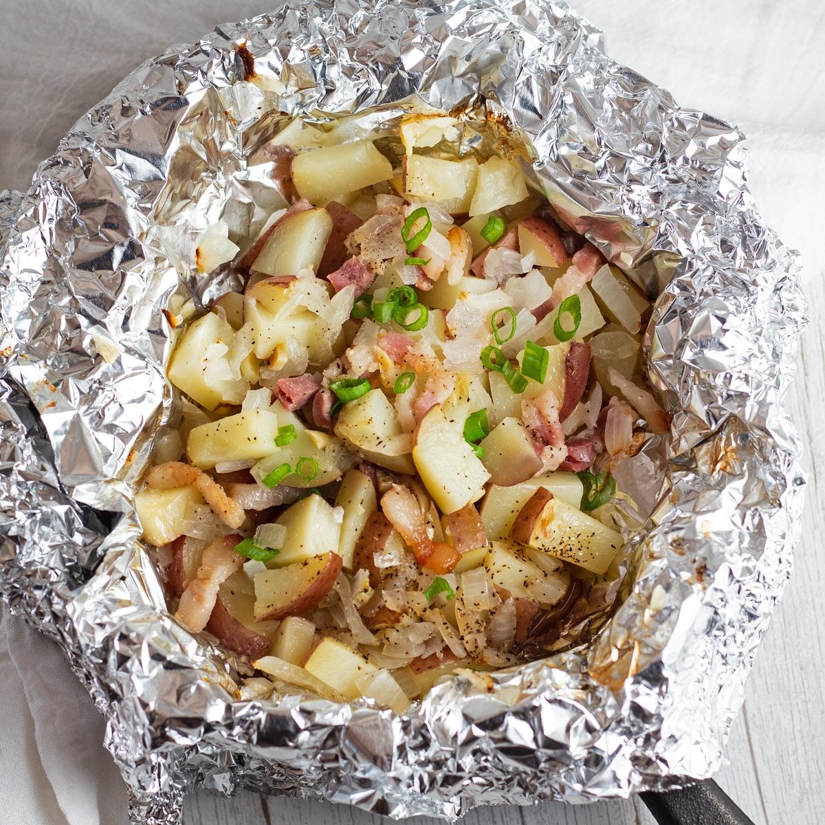 Potong kentang merah dalam foil dengan bacon, bawang merah, dan bawang putih.