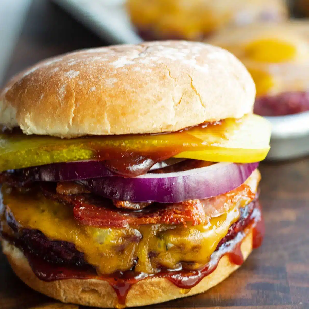 Uzený hamburger na opečené housce s kořením a podnosem s hamburgery v pozadí.