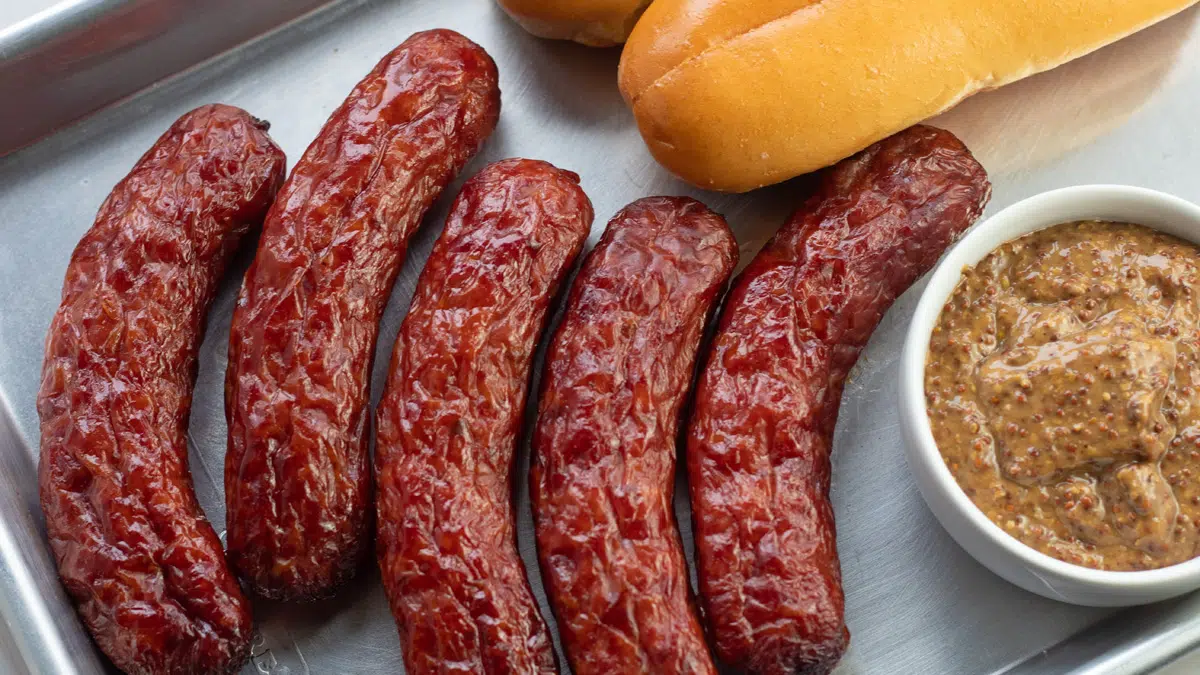 Wide image of smoked italian sausage on tray with buns and mustard.
