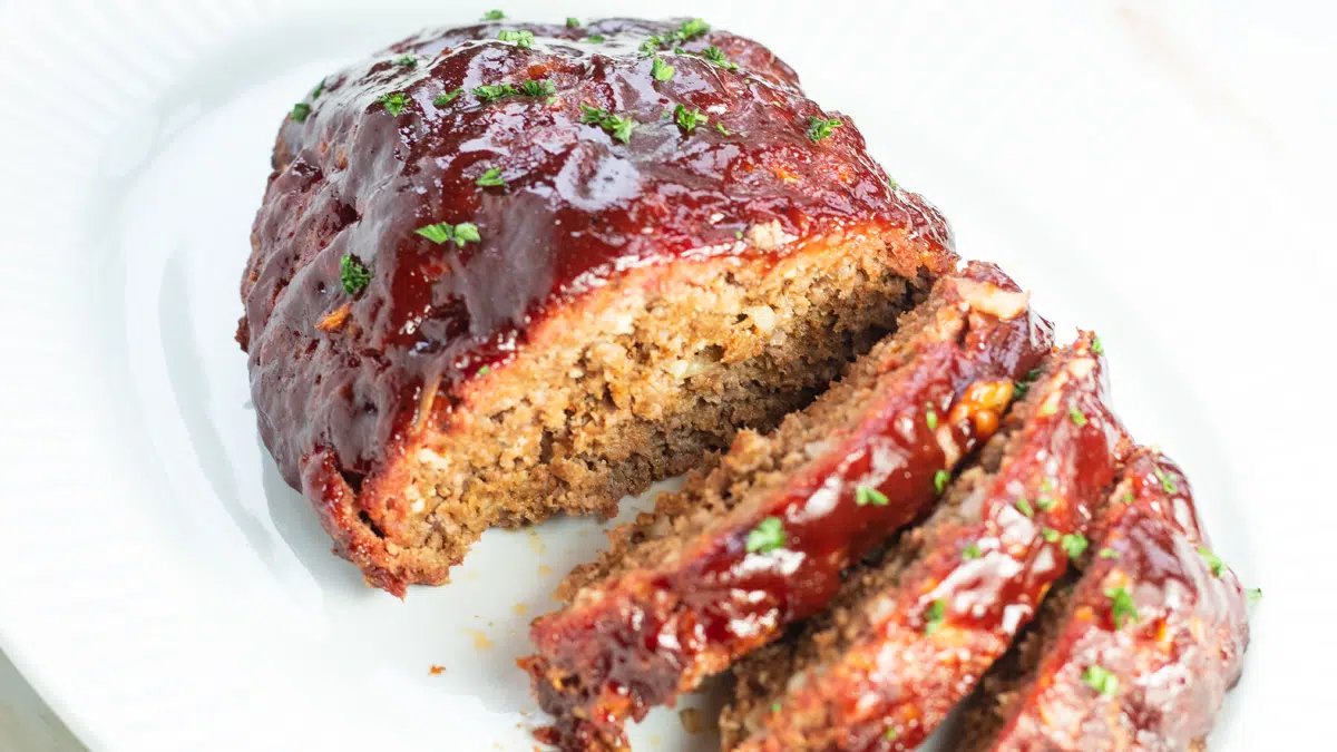 Wide image of the smoked meatloaf sliced and served on white platter.