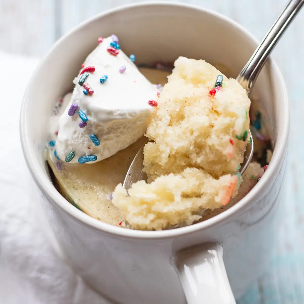Vanilla mug cake baked and topped with whipped cream and sprinkles.
