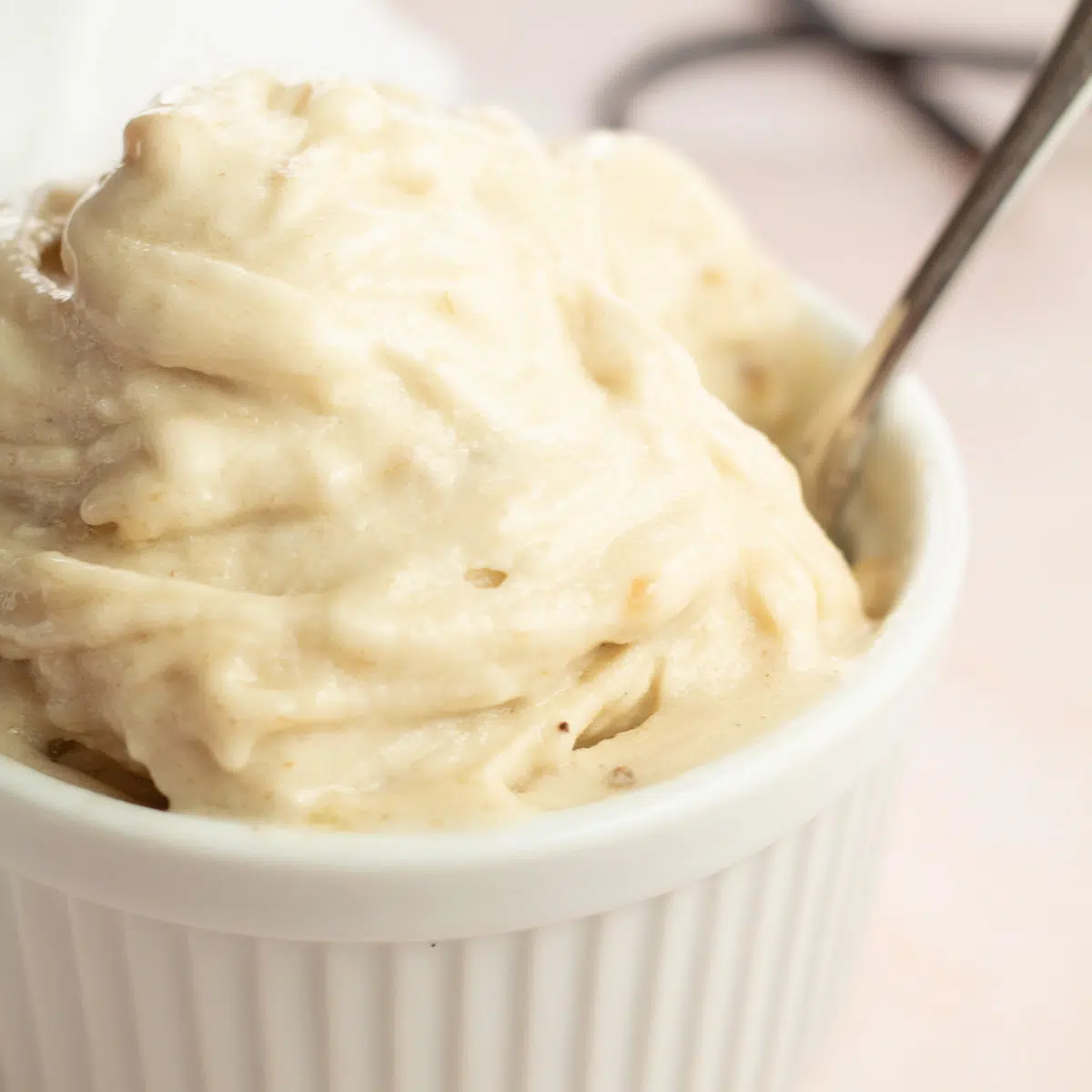 Vanilje dejlig fløde i hvid ramekin med ske i skålen og vaniljestang i baggrunden.