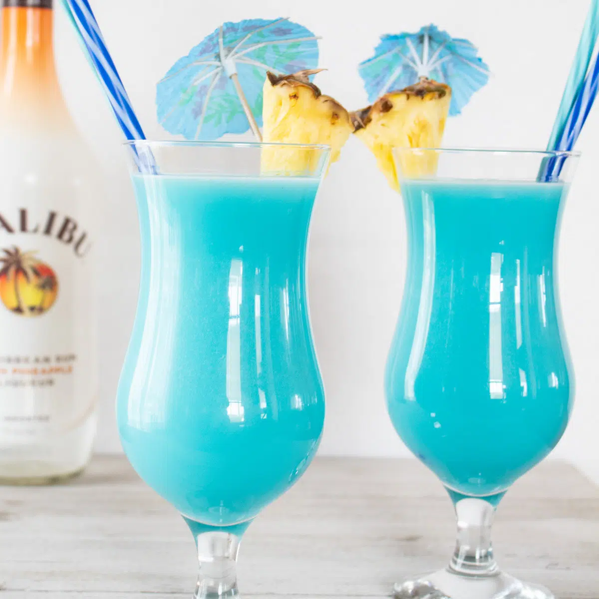 Frozen blue hawaiian cocktail served in hurrican glasses with pineapple garnish.