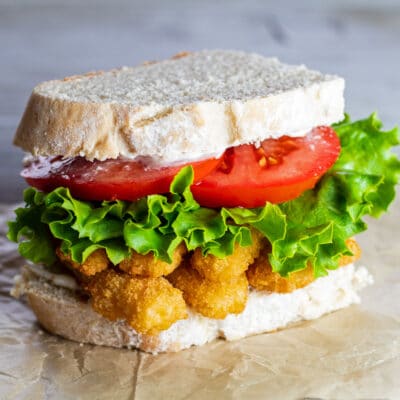 Fish stick sandwich with lettuce and tomato, on a plain background.
